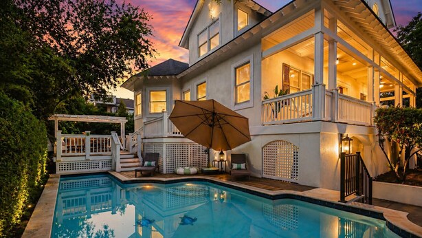 Ein zweistöckiges Haus mit Swimmingpool, Außenbereich mit Sitzgelegenheiten und einer überdachten Terrasse.