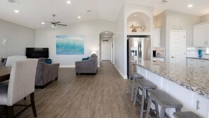 A spacious living area with a large TV, comfortable seating, a kitchen with a granite countertop, and a ceiling fan. - Blue Water Escape - 3 bedroom, 2 bath home that sleeps 8 - Easy Beach Access! (Crystal Beach)