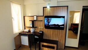 A compact hotel room with a wooden desk, a television mounted on the wall, a small seating area, and a window providing natural light. - Ridvan Otel (Bursa)