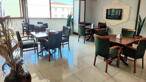 A spacious dining area with multiple tables and chairs, a large window offering a view of buildings, and a mounted television on the wall. - Ridvan Otel (Bursa)