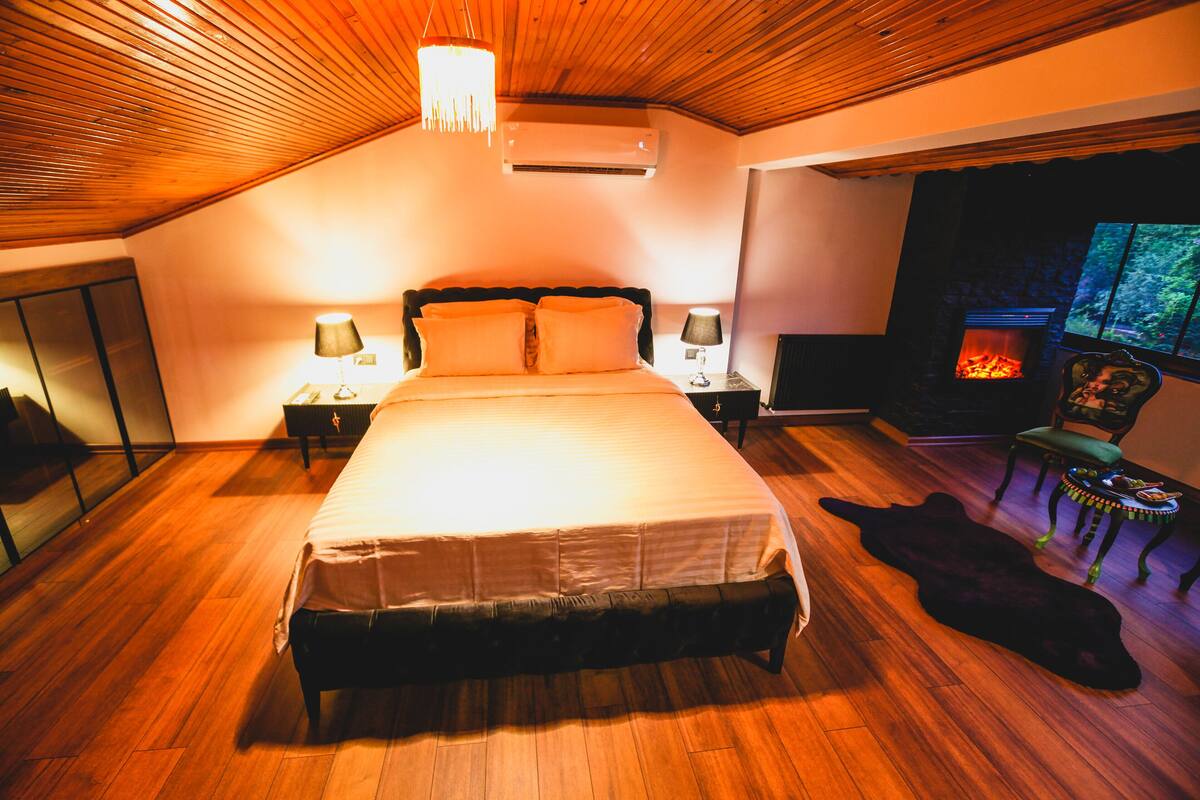 Ein Schlafzimmer mit einem großen Bett, einem Kamin, Holzböden und einer Decke mit Holzbalken.