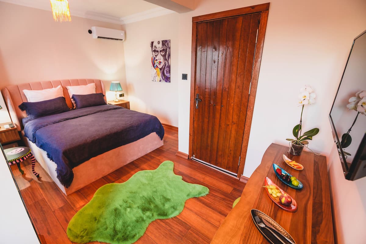 Ein Schlafzimmer mit einem Bett, einer Holztür, einem grünen Teppich und einem Esstisch mit Obst und Besteck.