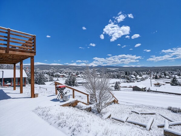 A snow-covered landscape with a wooden deck and a view of a town in the distance. - The Hilltop Suite — Mt Massive Views | Pet OK | EV Charger | Sleeps 4 (Leadville)