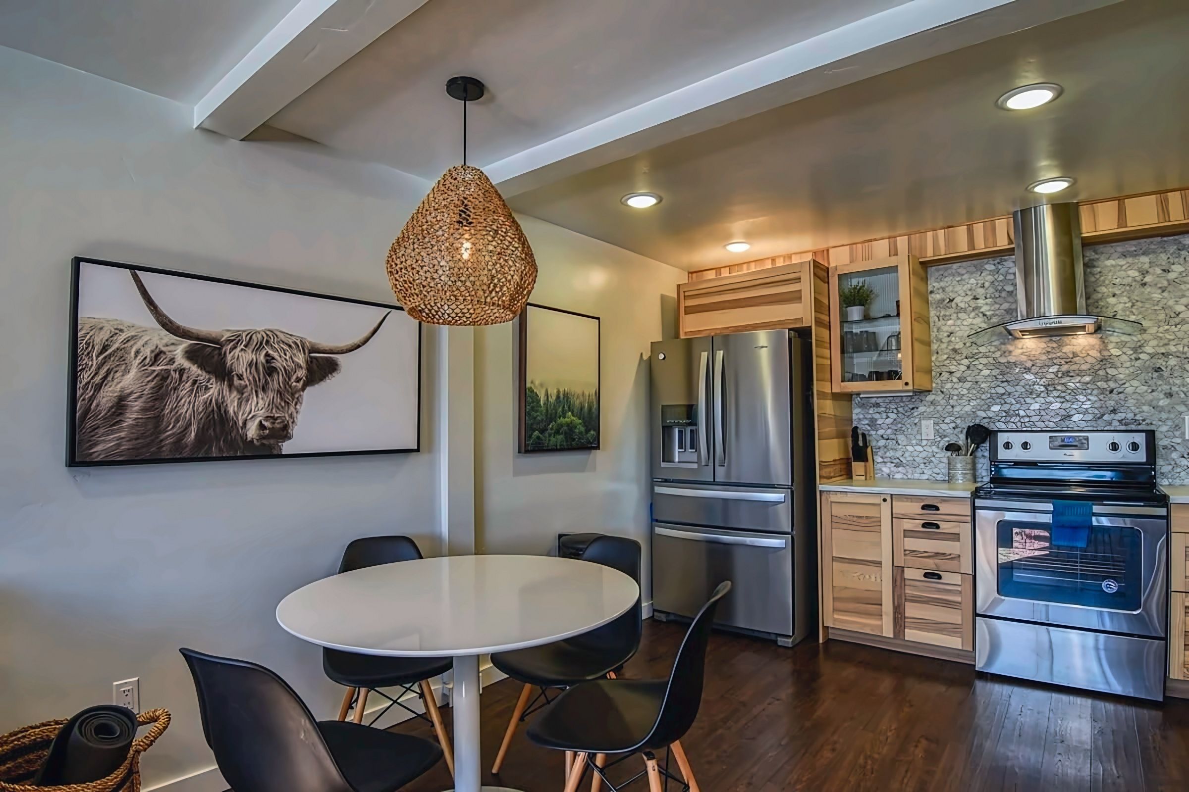 A modern kitchen with a dining area, featuring a round table, chairs, a hanging light fixture, and a refrigerator.