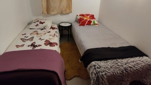 Ein kleines, schlichtes Zimmer mit zwei Einzelbetten, einem kleinen Tisch und einer Uhr.