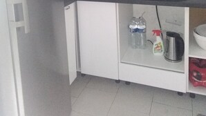 Eine kleine Küche mit weißen Schränken, einem Edelstahlkühlschrank, einer Mikrowelle und einem Spülbecken.