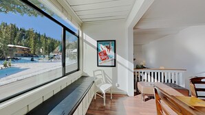 A room with a large window overlooking a snowy landscape, a framed poster on the wall, and a wooden bench. - Spacious 2 Bedroom Home with Pool, 3 Hot Tubs, Sauna! by RedAwning (Mammoth Lakes)