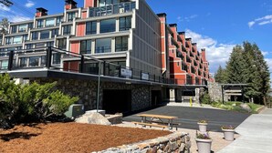 A multi-story hotel with a modern architectural design, featuring balconies, a covered entrance, and a landscaped outdoor area with a picnic table. - Deluxe Condo with Fireplace (Unit 623 at 1849) (Mammoth Lakes)