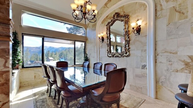 A spacious dining room with a large glass table, elegant chairs, a chandelier, a large mirror, and a view of mountains through large windows. - Deluxe Condo with Fireplace (Unit 623 at 1849) (Mammoth Lakes)