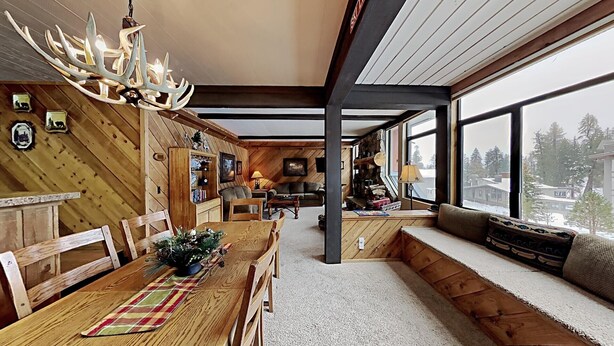 Ein gemütliches Blockhaus-Interieur mit einem Essbereich aus Holz, einem großen Fenster mit Blick auf den Wald und einem Kamin.