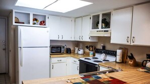 Una cocina compacta con gabinetes blancos, un microondas, una estufa y un lavamanos.