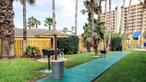 Un patio de hotel con un sendero verde, palmeras y asientos al aire libre.