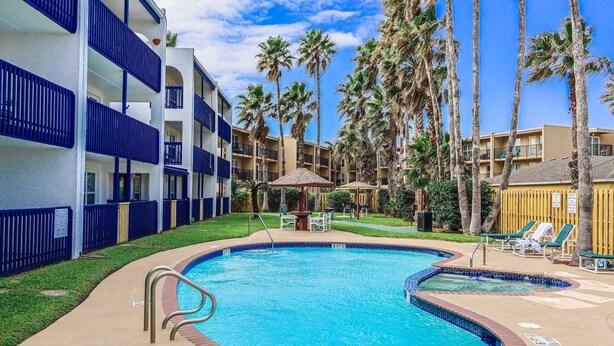 Un hotel con piscina rodeada de palmeras y un cielo azul despejado.