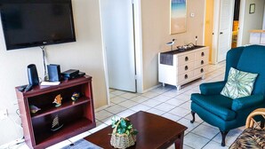 Una sala de estar con televisor, una unidad de entretenimiento de madera, un sillón azul y una mesita con una cesta.