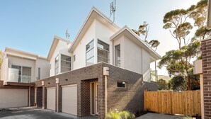 A modern two-story residential building with a garage, a brick facade, and a wooden fence. - Bay & Relax (Apollo Bay)