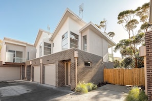 A modern two-story residential building with a garage, a brick facade, and a wooden fence. - Bay & Relax (Apollo Bay)