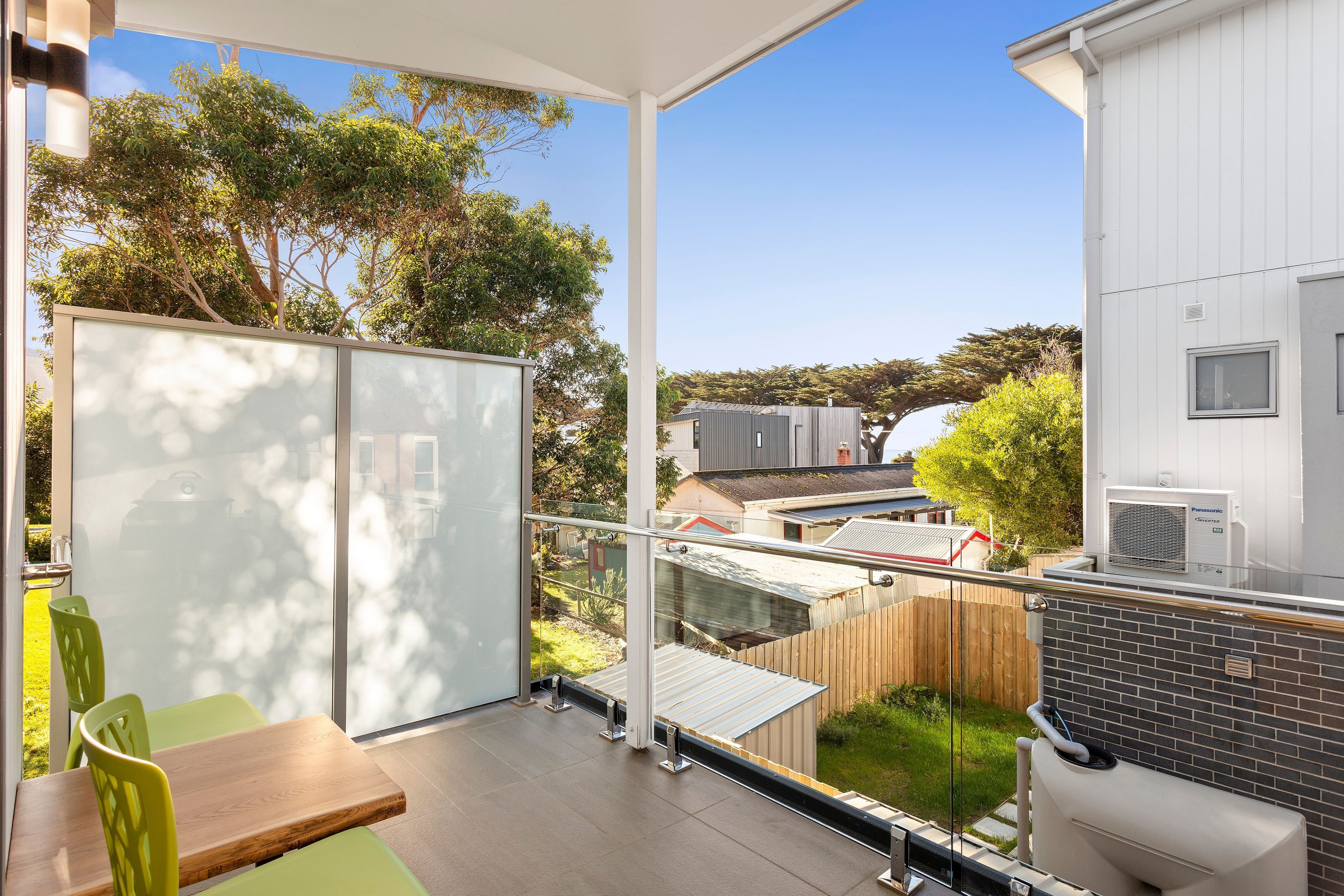 Ein Balkon mit Glastür, einem Holztisch und Stühlen, mit Blick auf einen Garten und Gebäude.