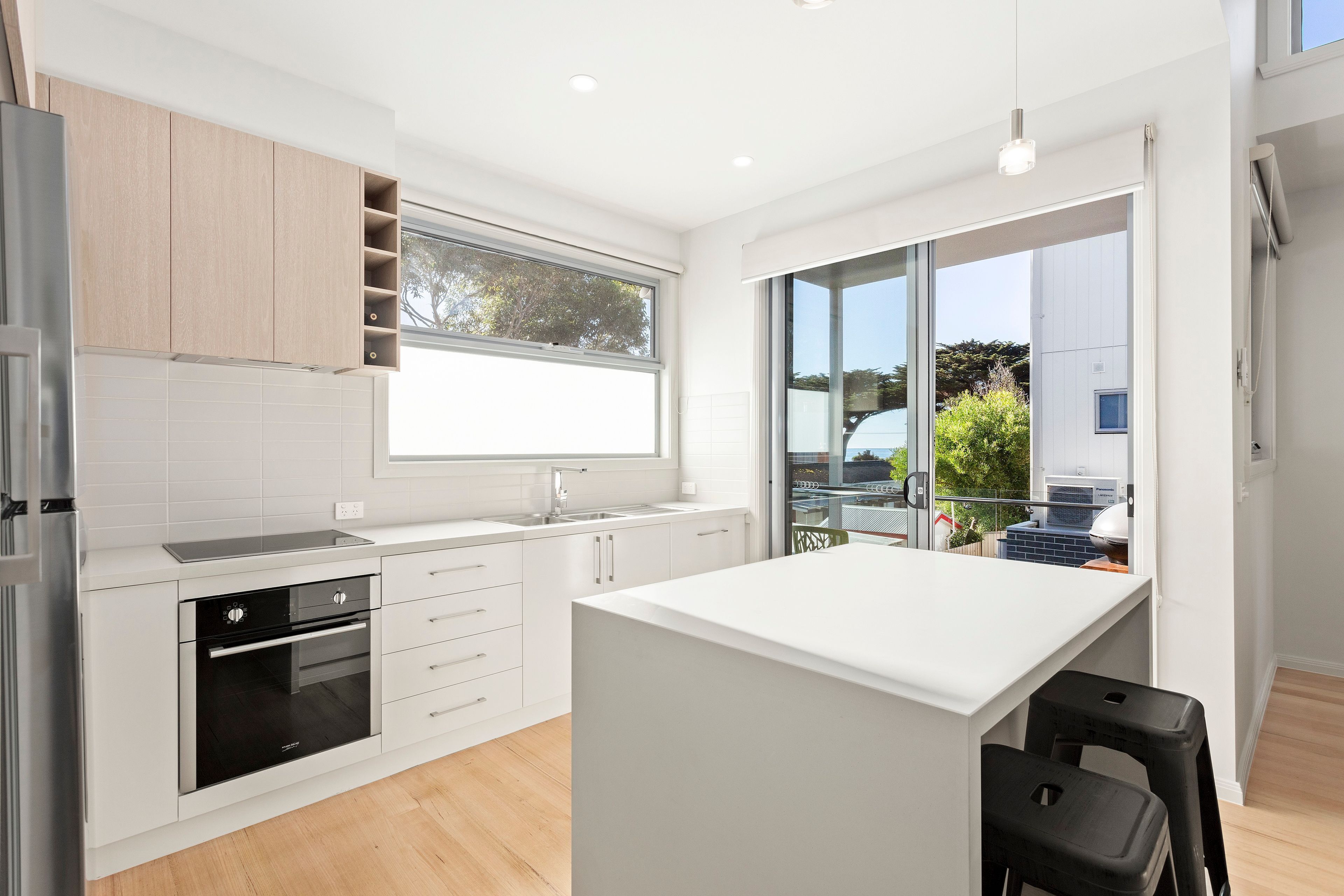 A modern kitchen with a central island, built-in oven, and a large window.