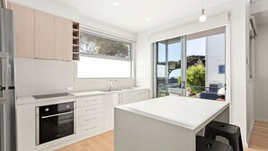 A modern kitchen with a central island, built-in oven, and a large window. - Bay & Relax (Apollo Bay)