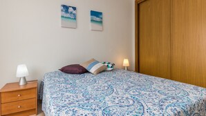 A bedroom with a bed, a nightstand, a lamp, two wall art pieces, and a wooden wardrobe.