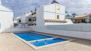 A swimming pool with a tiled deck, surrounded by white buildings with balconies and satellite dishes.
