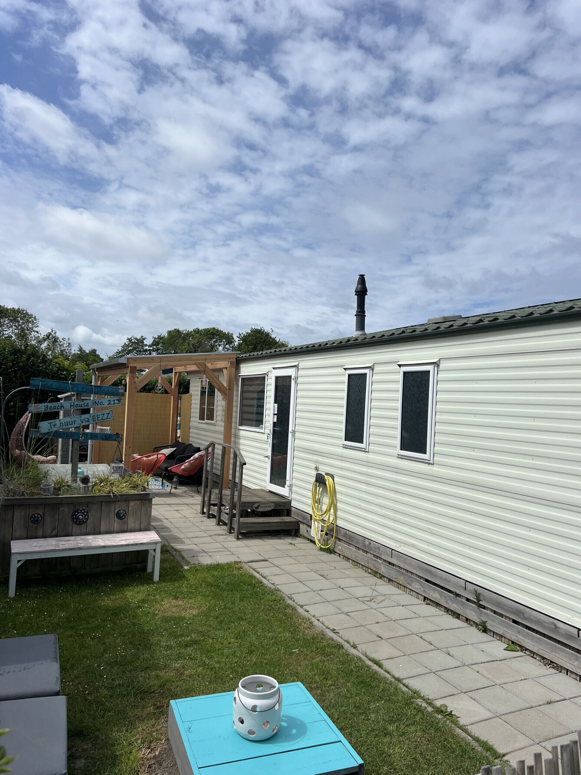 A mobile home with a covered porch, a small deck, and a hose coiled against the side.