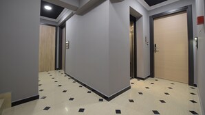 Un corridoio con pavimento piastrellato, una porta in legno e una porta dell'ascensore chiusa.