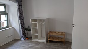 A room with a wooden bench, a white shelving unit, a potted plant, and a window with a curtain. - Vacations in the historic city center of Zittau - IO19 / 1L (Zittau)