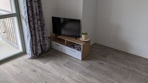 A modern living room with a flat-screen TV on a wooden stand, a potted plant, and a sliding door with patterned curtains. - Vacations in the historic city center of Zittau - IO19 / 1L (Zittau)