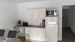 A compact kitchen with a microwave, coffee maker, and a sink. There is a dining table with chairs and a small shelf above the counter. - Vacations in the historic city center of Zittau - IO19 / 1L (Zittau)