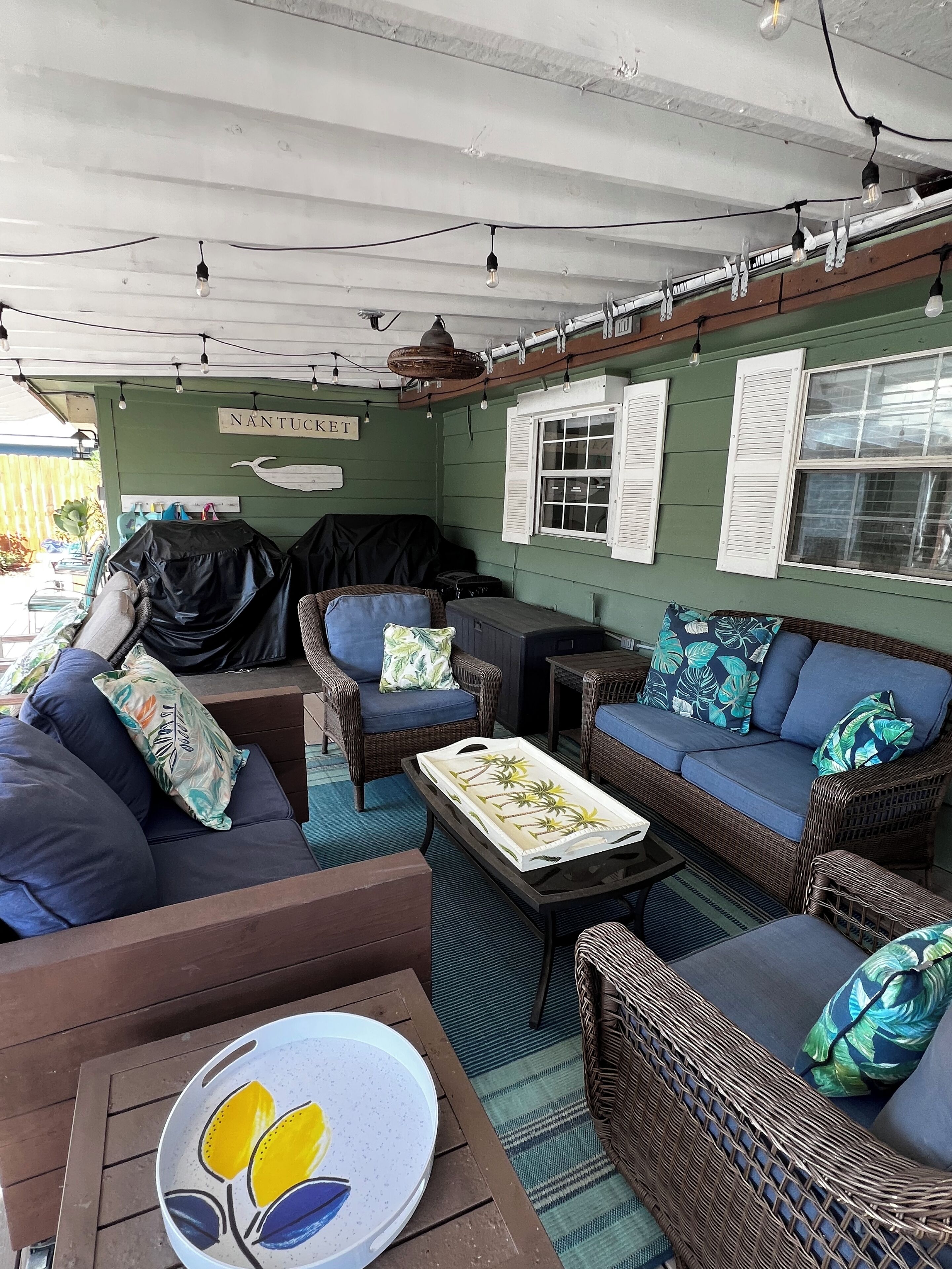 A covered outdoor seating area with wicker furniture, a table, and string lights.