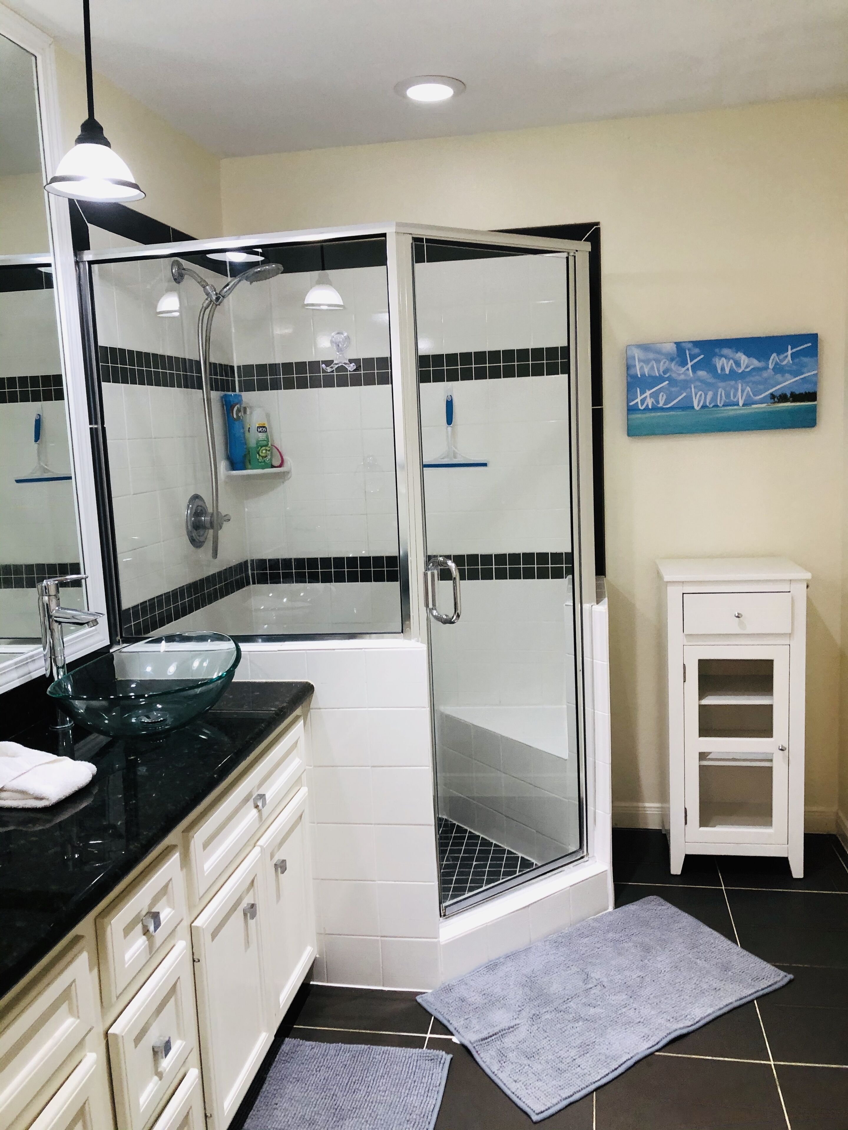 A modern bathroom with a glass-enclosed shower, a glass bowl sink, white cabinetry, and a small white cabinet.