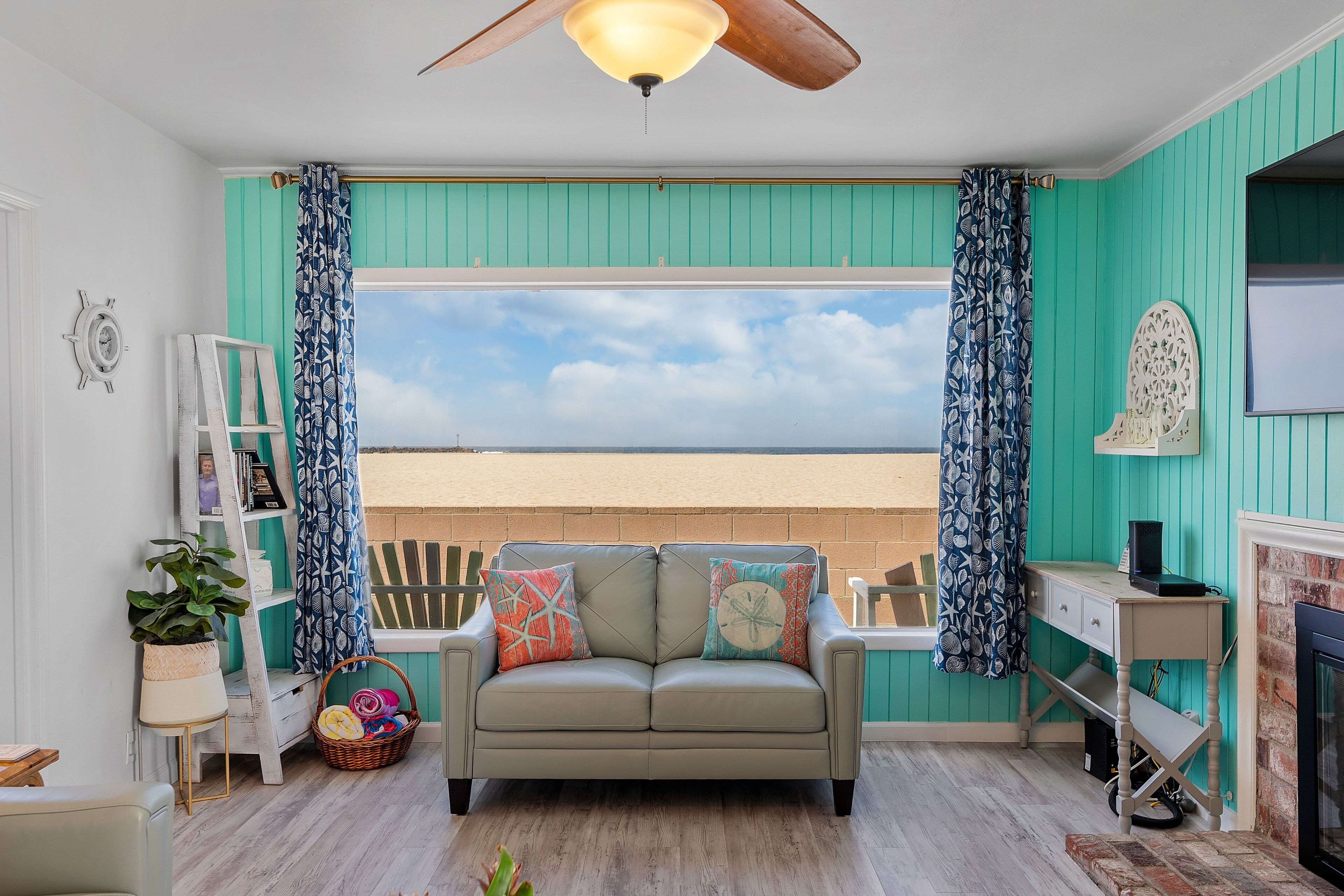 Un salon chaleureux avec un mur d’accent de couleur turquoise, une grande fenêtre offrant une belle vue, un ventilateur de plafond et une cheminée.