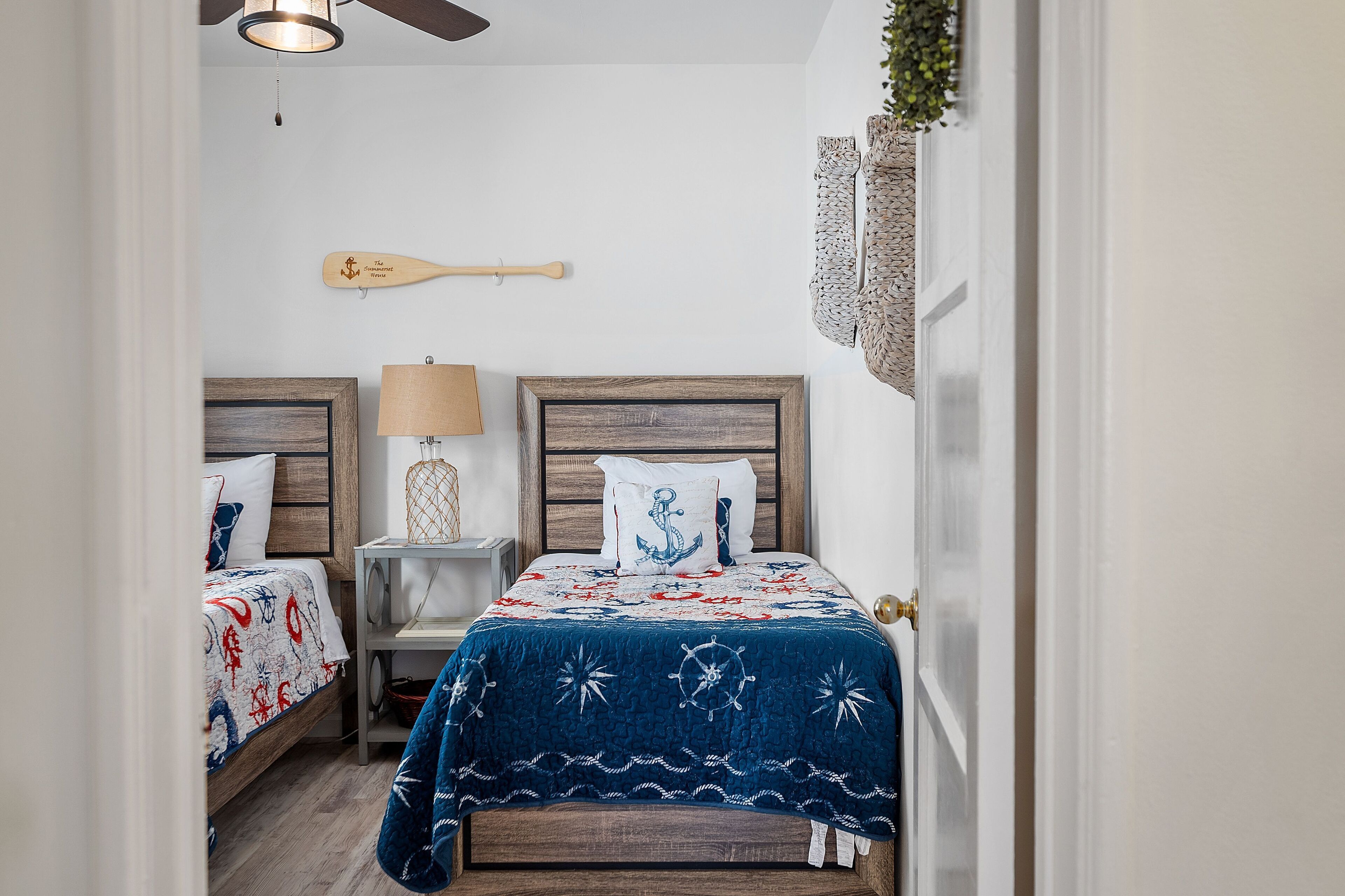 A bedroom with two beds, each with a wooden headboard, a nightstand with a lamp, and a wall-mounted shelf.