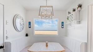 Zona pranzo con tavolo e panche in legno, orologio a parete, vista sulla spiaggia e lampadario.