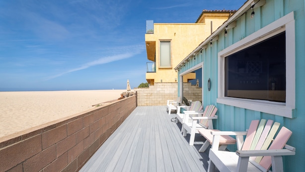 Un patio in legno con poltrone Adirondack bianche, un muro in mattoni e un edificio con facciata blu.
