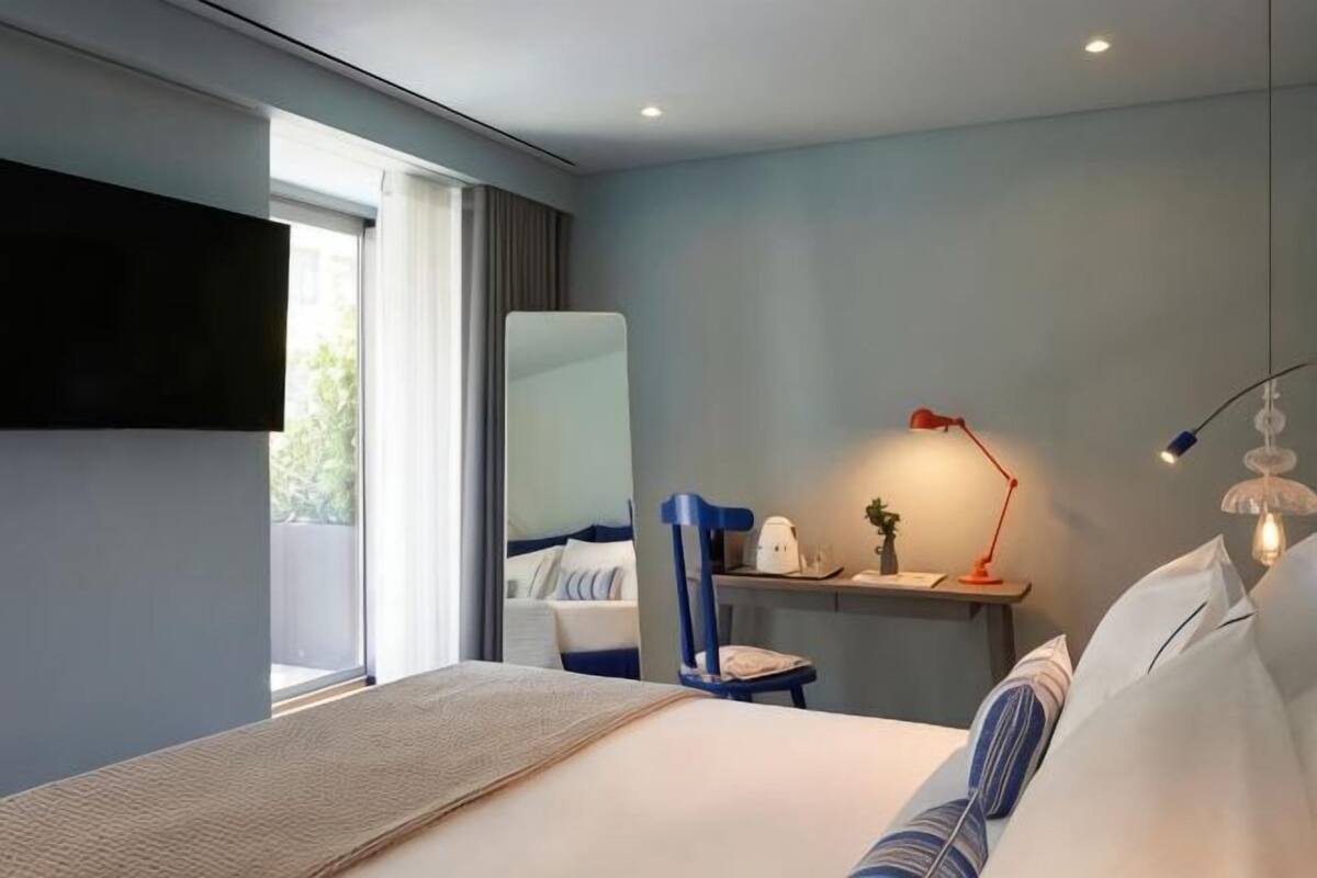 A modern hotel room with a bed, a desk, a chair, a TV, and a window.