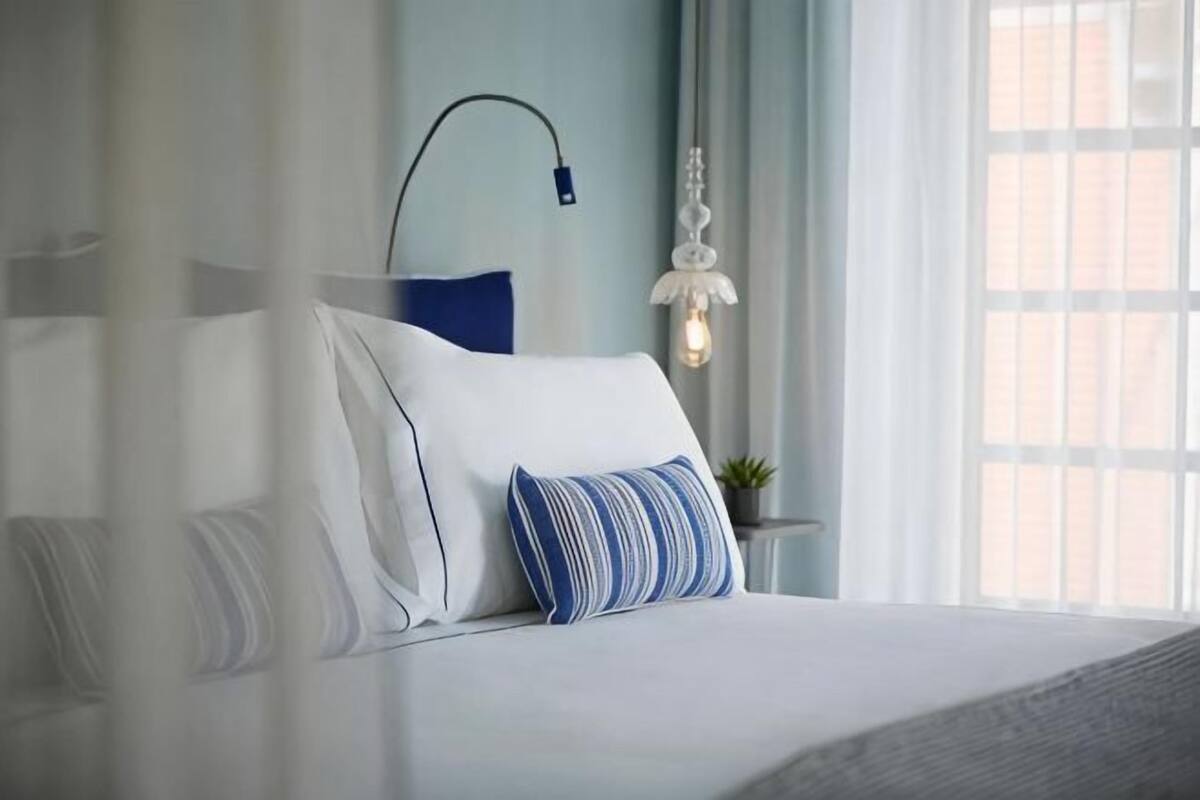 A neatly made bed with pillows, a bedside lamp, and a window with curtains.
