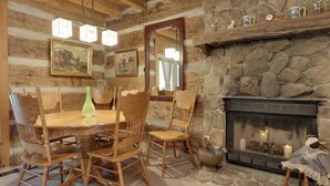 Un comedor rústico de madera con chimenea de piedra, sillas de madera, una mesa redonda y decoración colgante en la pared.