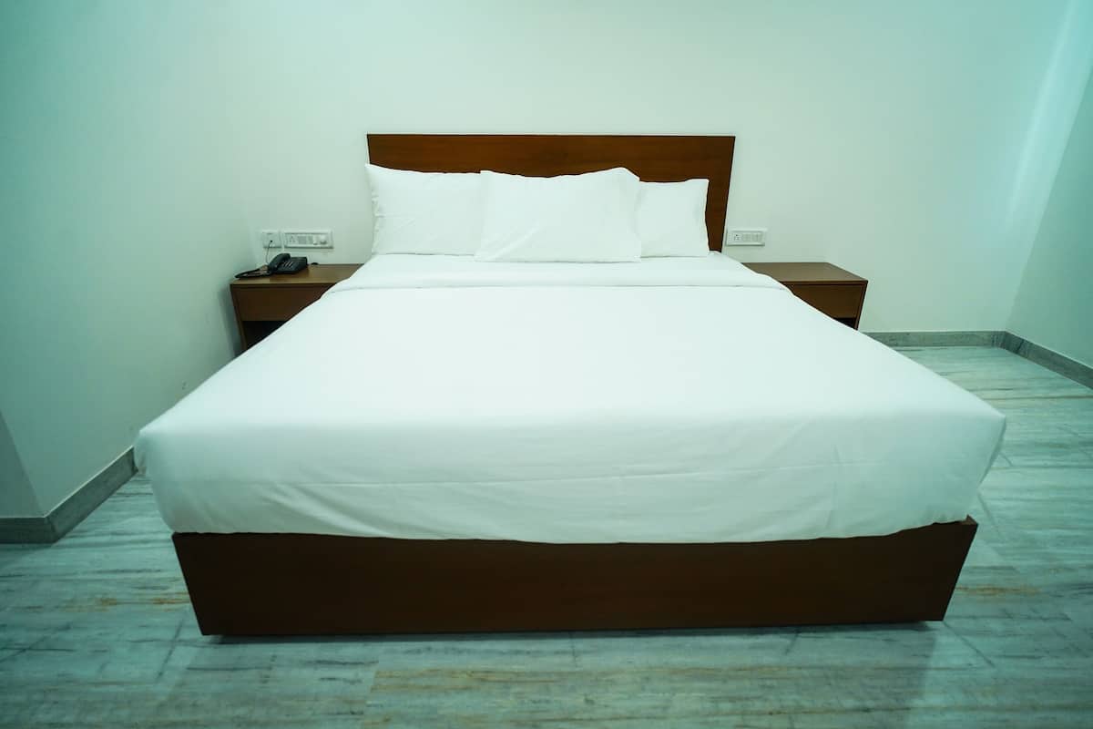 A neatly made bed with white linens in a room with a wooden headboard.