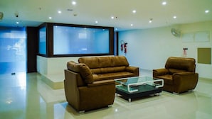 A modern lobby with a brown leather sofa, a glass coffee table, and a large blue-framed screen.