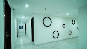 A long, narrow hallway with a polished marble floor and white walls. The hallway has several doors on one side and circular wall decorations on the other.