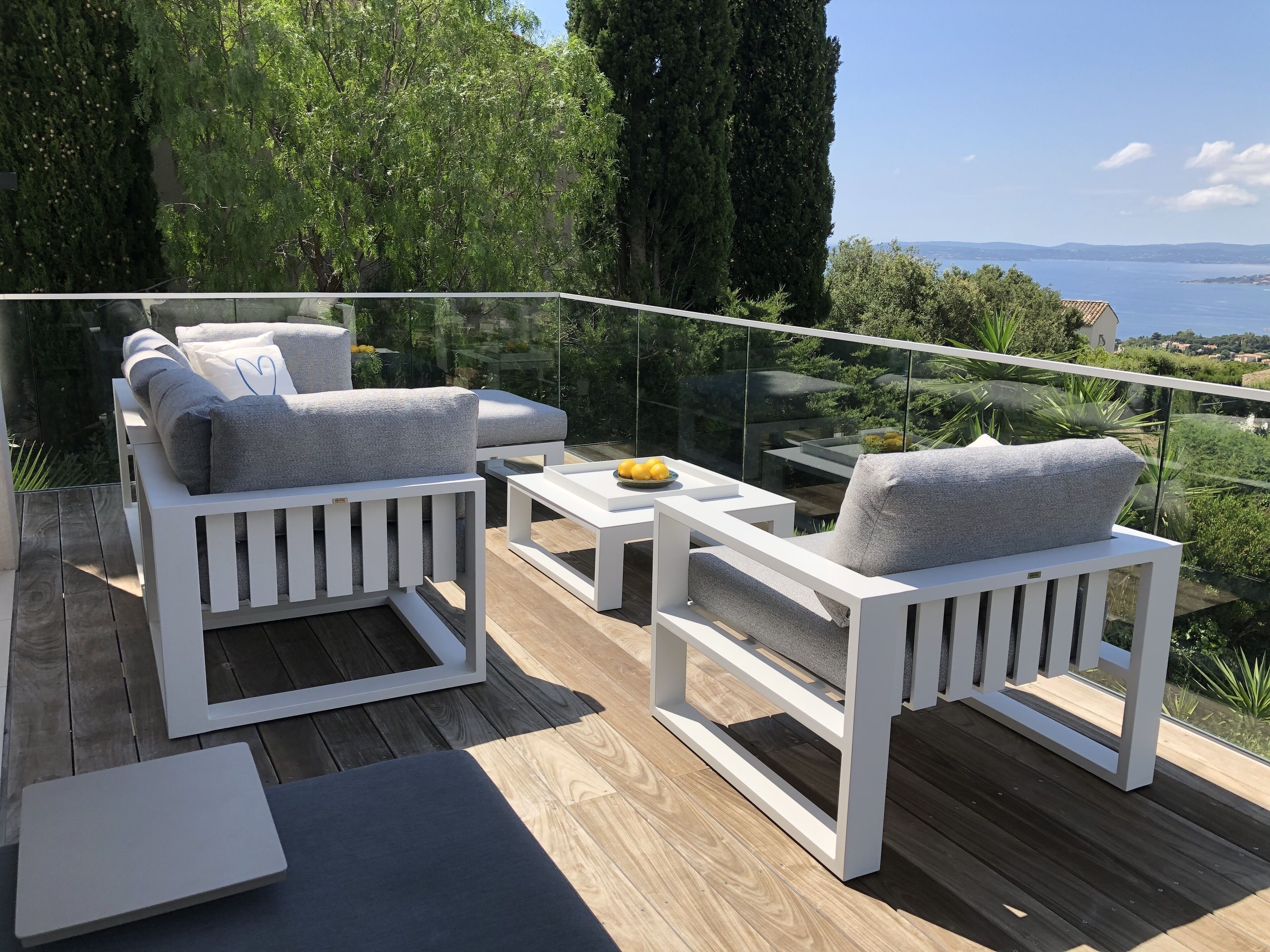 A balcony with white furniture, a glass railing, and a view of the sea.