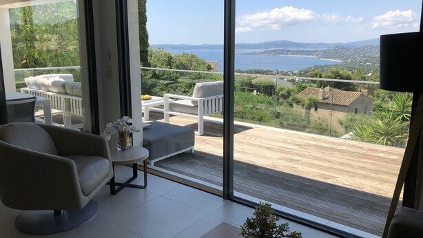 Ein modernes Wohnzimmer mit einer großen Schiebetür zu einem Balkon mit herrlichem Meer- und Hügelblick.
