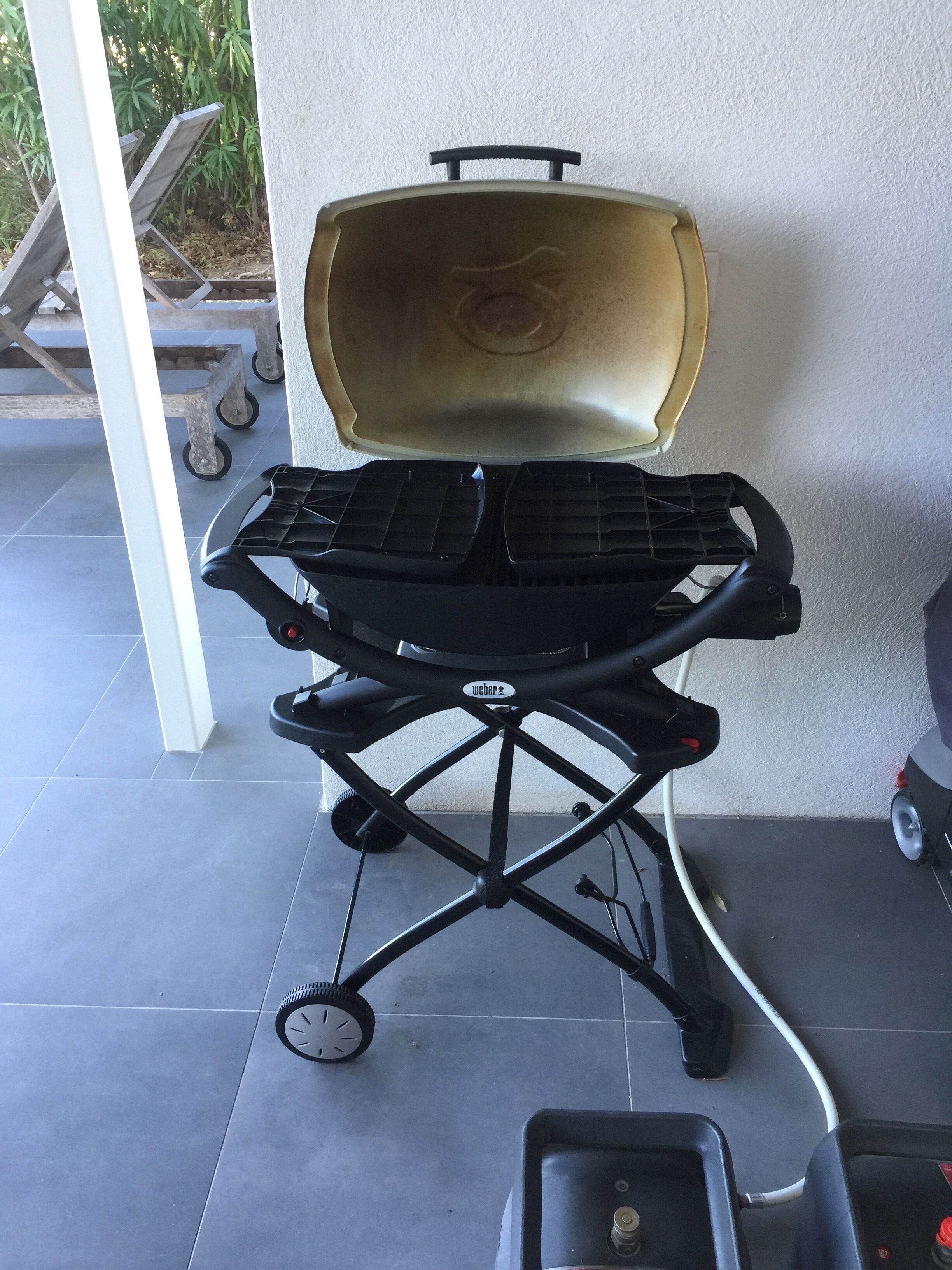 A portable grill with wheels, positioned on a tiled patio.