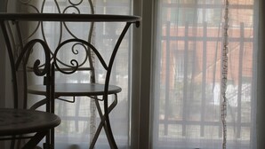 Una habitación con una silla y una mesa de metal cerca de una ventana con cortinas traslúcidas.