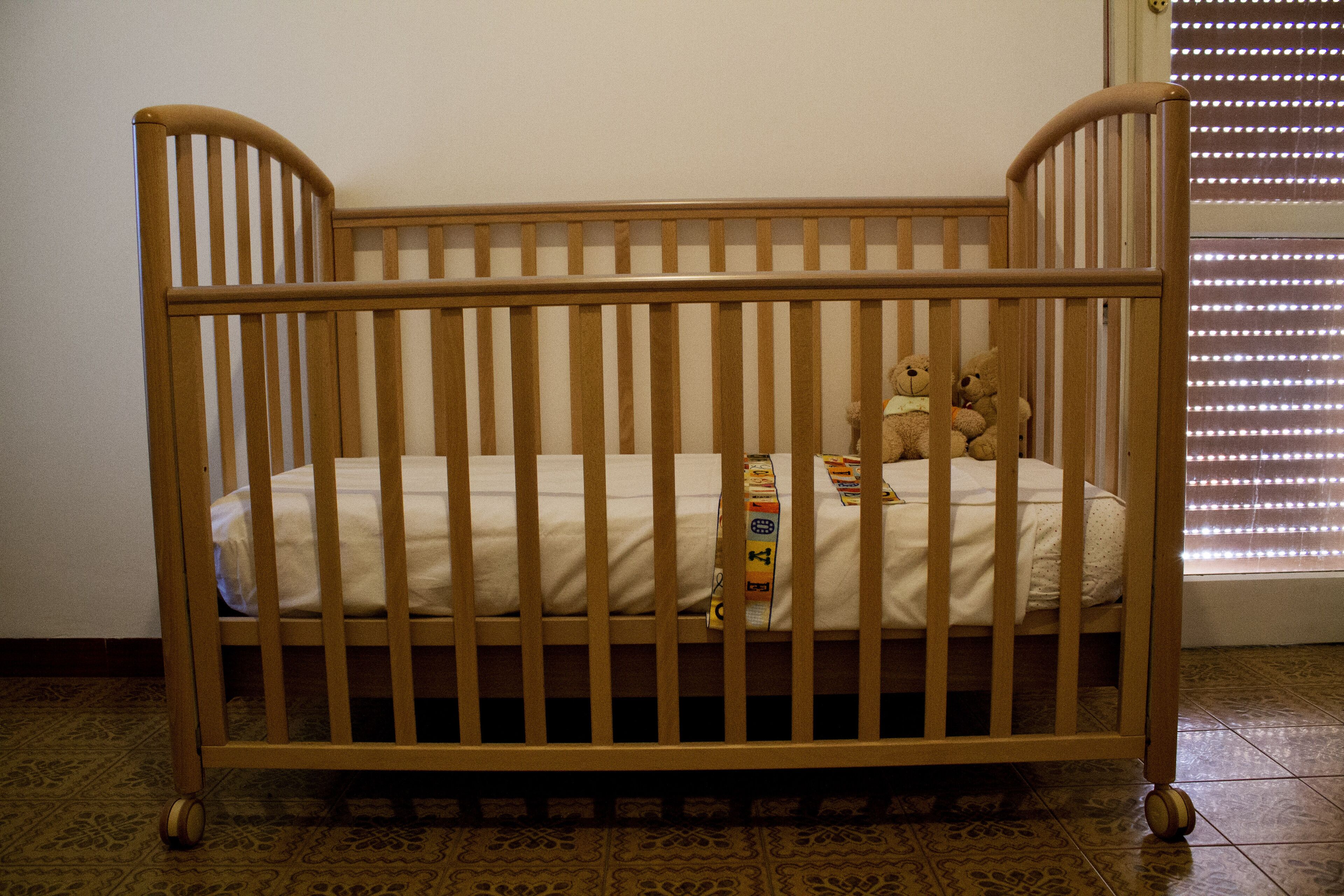 A wooden crib with a mattress and two teddy bears.