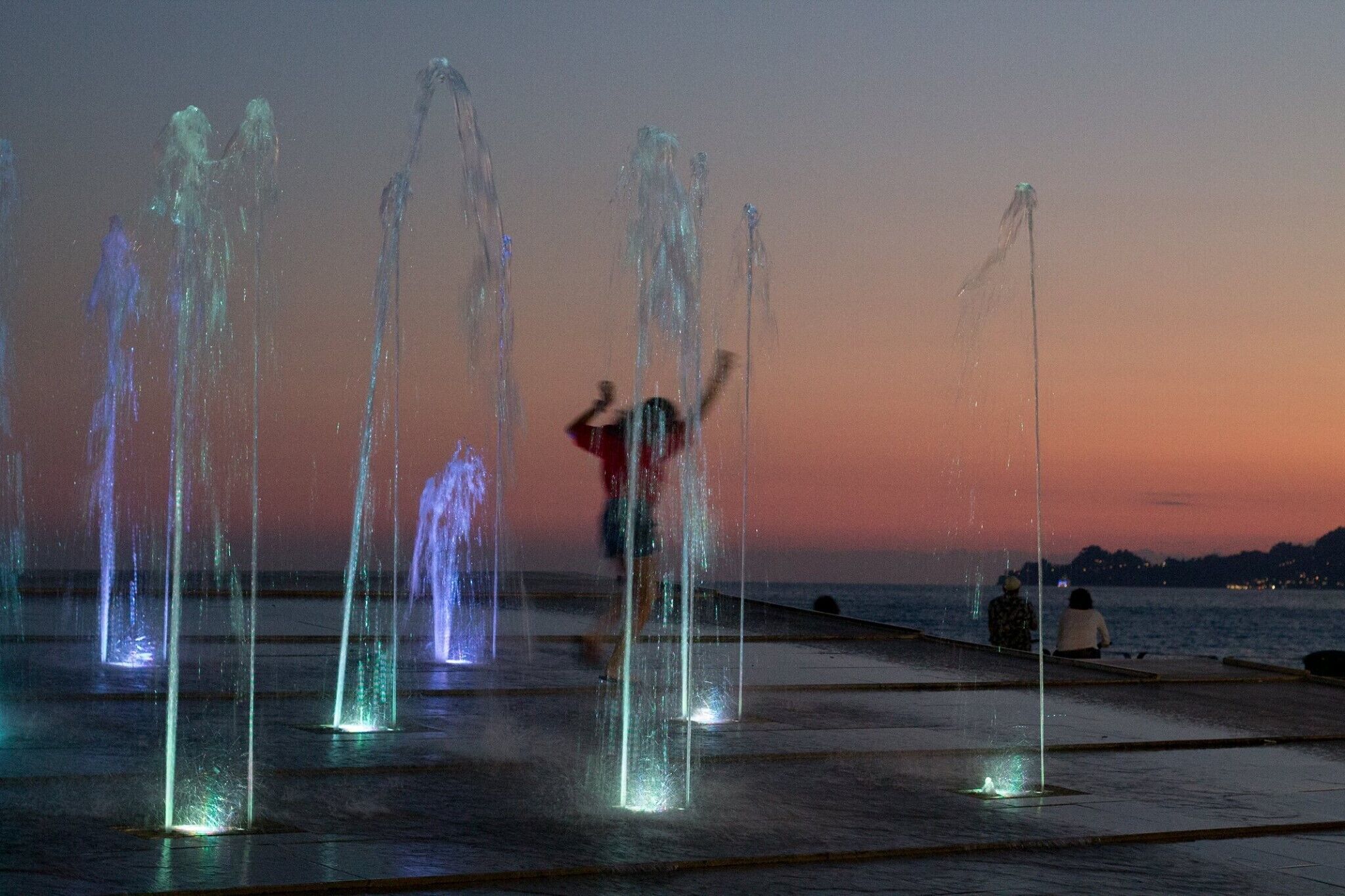 A waterfront with water jets and a sunset.