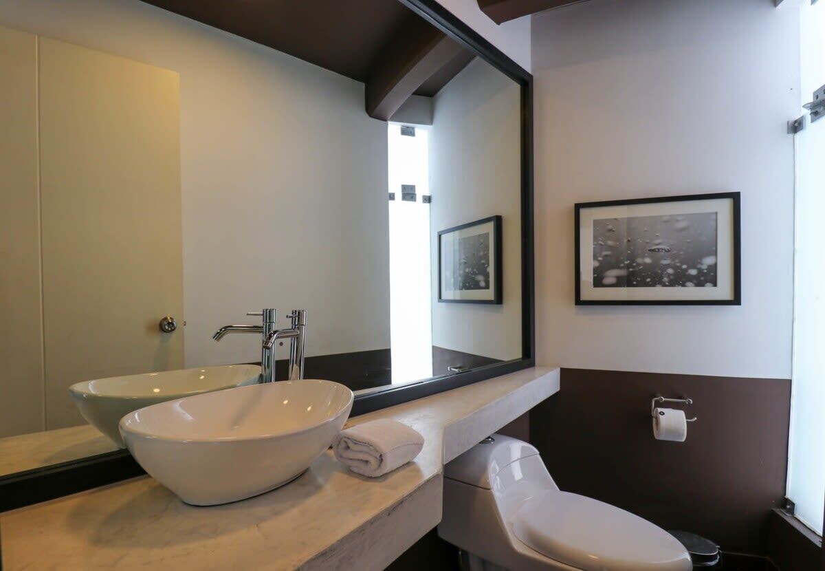 A modern bathroom with a large mirror, a white sink, and a toilet.