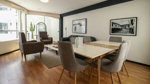 Un comedor moderno con mesa de madera y sillas grises tapizadas, una mesa de centro de vidrio y cuadros enmarcados en la pared.